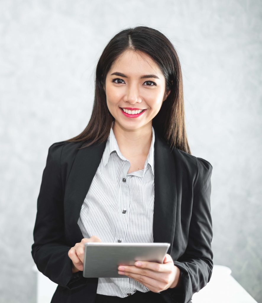 Portrait young Asian businesswoman holding tablet/smartphone in formal suit in office with copy space